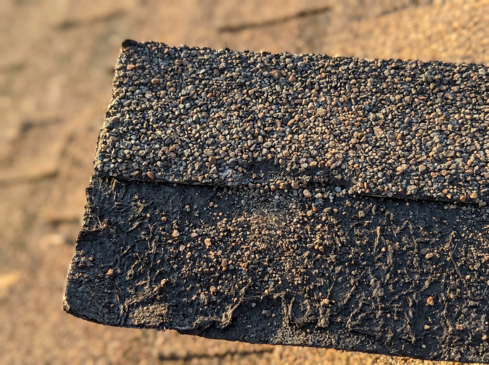Macro close-up of an aged asphalt shingle showing granule loss and exposed black asphalt mat below
